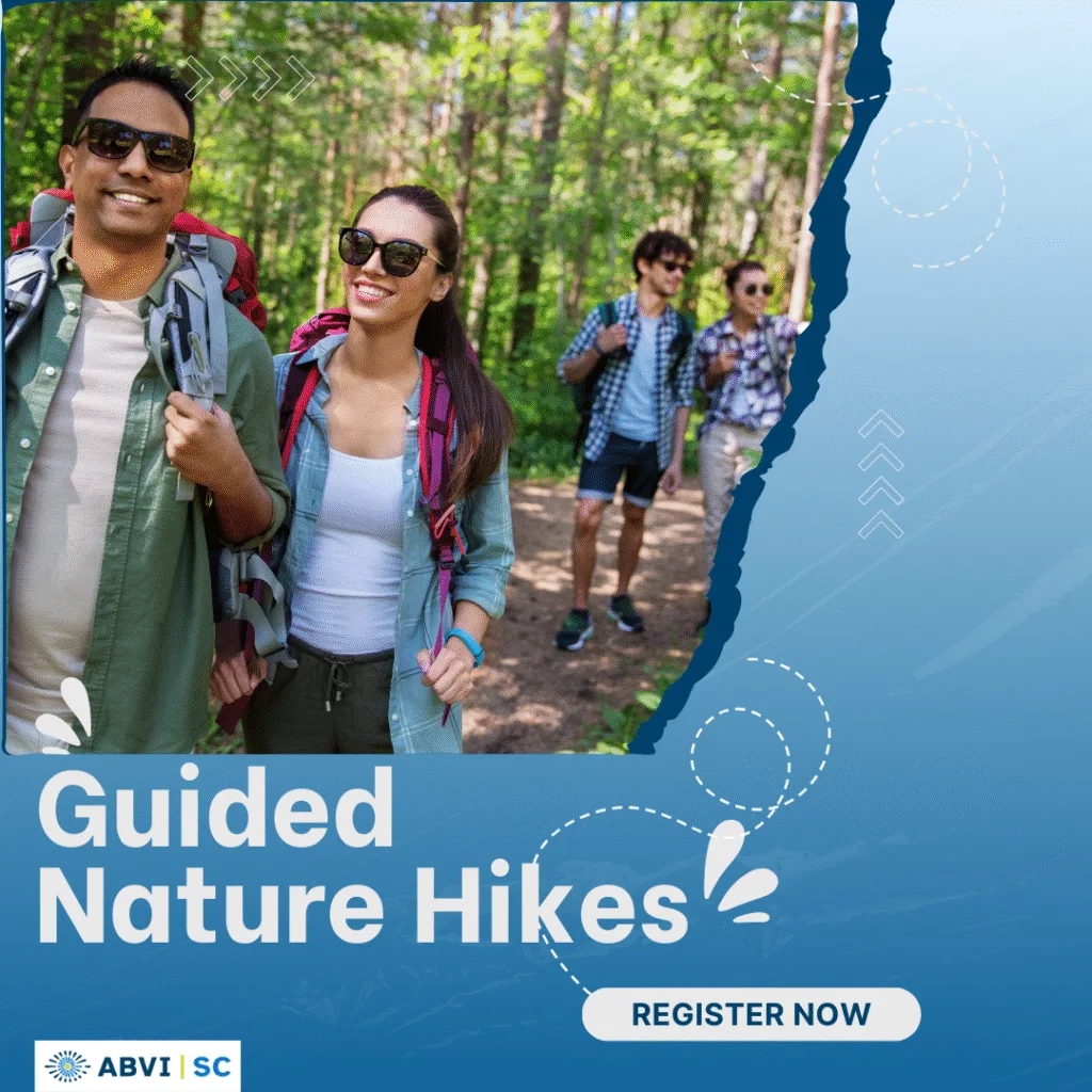 Four adults, each wearing sunglasses and a backpack, walk happily walk together under a canopy of trees on a nature trail