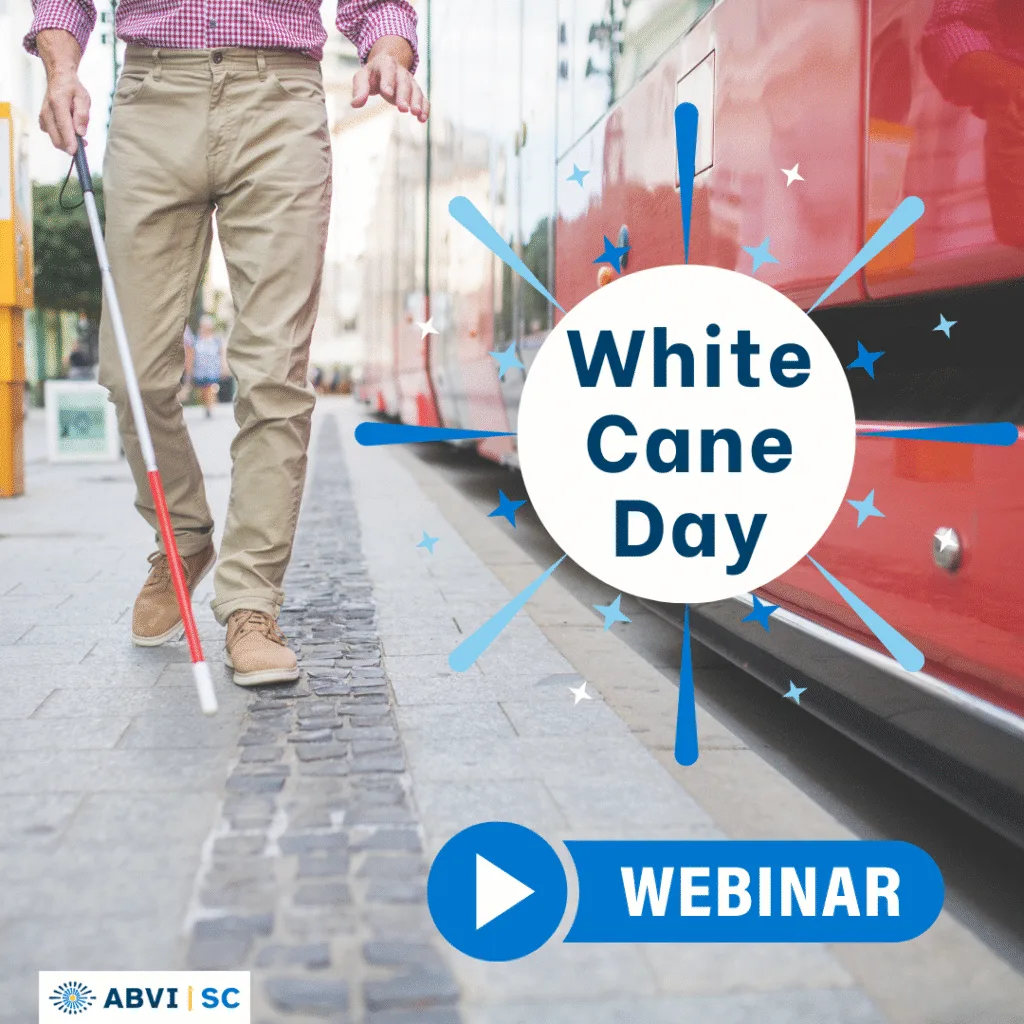 Man uses a white cane to walk down a sidewalk alongside a city bus.