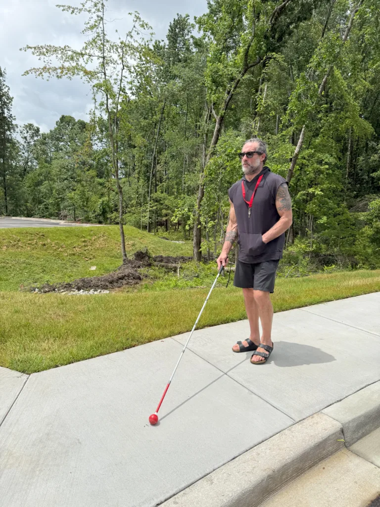 Man walking on sidewalk with white cane.