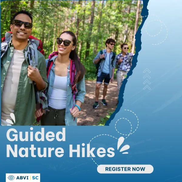 Four adults, each wearing sunglasses and a backpack, walk happily walk together under a canopy of trees on a nature trail