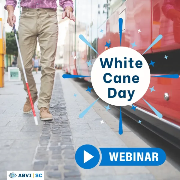 Man uses a white cane to walk down a sidewalk alongside a city bus.